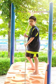 Young asian boy hang the yellow bar by his hand to exercise at out door playground under the big tree