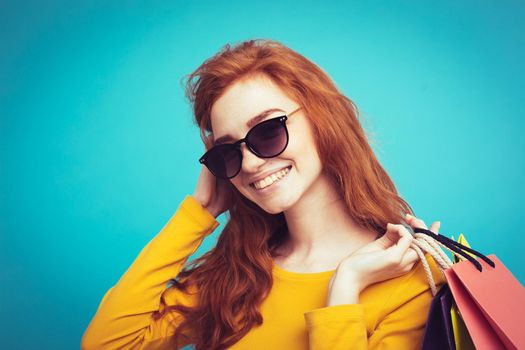 Shopping Concept - Close up Portrait young beautiful attractive redhair girl smiling looking at camera with shopping bag. Blue Pastel Background. Copy space.