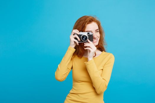 Travel and People Concept - Headshot Portrait of happy ginger red hair girl with playing with vintage camera in happy expression. Pastel blue background. Copy Space.