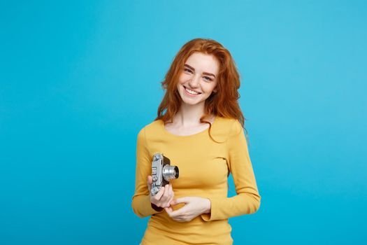 Close up Portrait young beautiful attractive ginger girl happy smiling with vintage camera and ready to travel. Isolated on Blue Pastel Background. Copy space.