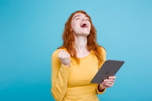 People and Technology Concept - Close up Portrait young beautiful attractive redhair girl happy smiling on digital table with wining something. Blue Pastel Background. Copy space.