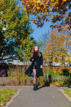 A woman with long hair walks alone along a path in an autumn park. Autumn season concept.