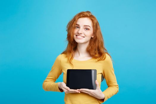 Close up Portrait young beautiful attractive redhair girl smiling showing digital tablet screen on black. Blue Pastel Background. Copy Space.