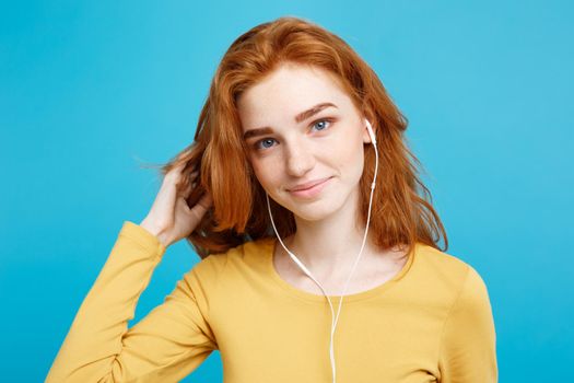 Lifestyle concept - Portrait of cheerful happy ginger red hair girl enjoy listening to music with headphones joyful smiling to camera. Isolated on Blue Pastel Background. Copy space.