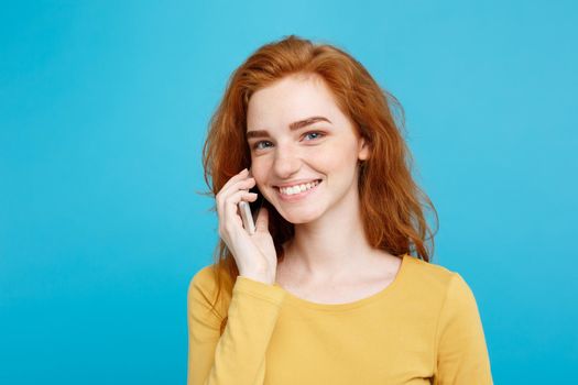 Lifestyle and Technology concept - Portrait of cheerful happy ginger red hair girl with joyful and exciting talking with friend by mobile phone. Isolated on Blue Pastel Background. Copy space.