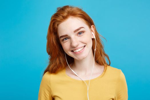 Lifestyle concept - Portrait of cheerful happy ginger red hair girl enjoy listening to music with headphones joyful smiling to camera. Isolated on Blue Pastel Background. Copy space.