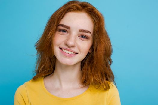 Headshot Portrait of happy ginger red hair girl with freckles smiling looking at camera. Pastel blue background. Copy Space.