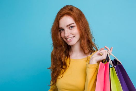 Shopping Concept - Close up Portrait young beautiful attractive redhair girl smiling looking at camera with shopping bag. Blue Pastel Background. Copy space.