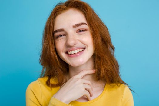 Headshot Portrait of happy ginger red hair girl with freckles smiling looking at camera. Pastel blue background. Copy Space.