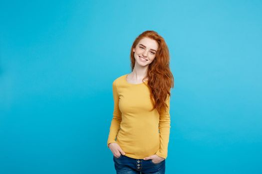 Portrait of young beautiful ginger woman with freckles cheerfuly smiling looking at camera. Isolated on pastel blue background. Copy space.