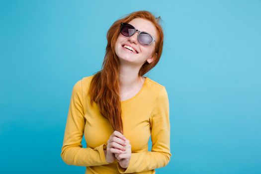 Portrait of happy ginger red hair girl with freckles smiling looking at camera. Pastel blue background. Copy Space.