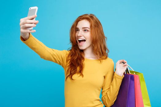 Shopping Concept - Close up Portrait young beautiful attractive redhair girl smiling looking at camera with white shopping bag and selfie. Blue Pastel Background. Copy space.