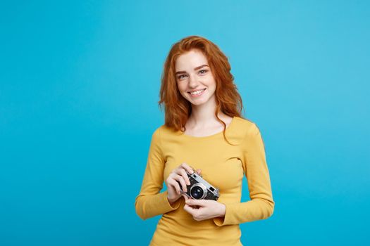 Close up Portrait young beautiful attractive ginger girl happy smiling with vintage camera and ready to travel. Isolated on Blue Pastel Background. Copy space.