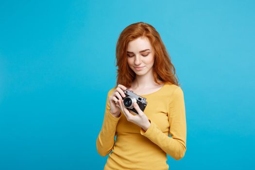 Travel and People Concept - Headshot Portrait of happy ginger red hair girl with playing with vintage camera in happy expression. Pastel blue background. Copy Space.