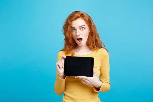 Business Concept - Close up Portrait young beautiful attractive redhair girl smiling showing digital tablet screen on black. Blue Pastel Background.