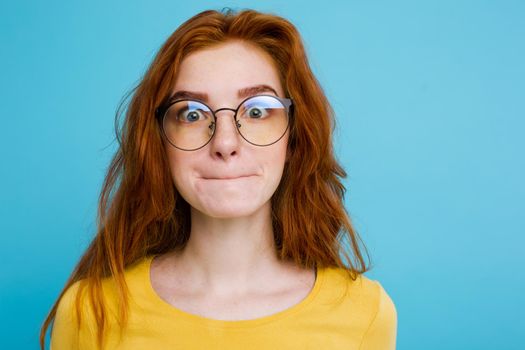 Headshot Portrait of happy ginger red hair girl with funny face looking at camera. Pastel blue background. Copy Space.