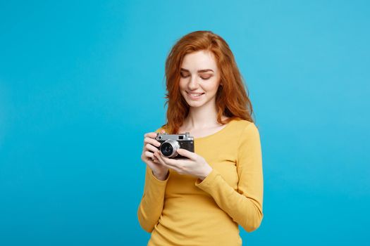 Travel and People Concept - Headshot Portrait of happy ginger red hair girl with playing with vintage camera in happy expression. Pastel blue background. Copy Space.