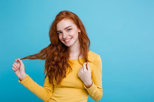 Portrait of happy ginger red hair girl with freckles smiling looking at camera. Pastel blue background. Copy Space.