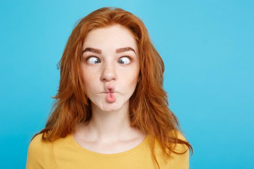 Headshot Portrait of happy ginger red hair girl with funny face looking at camera. Pastel blue background. Copy Space.