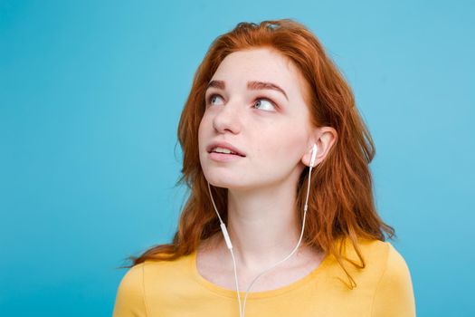 Lifestyle concept - Portrait of cheerful happy ginger red hair girl enjoy listening to music with headphones joyful smiling to camera. Isolated on Blue Pastel Background. Copy space.