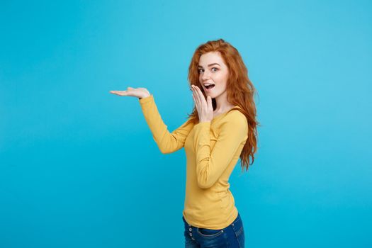 Fun and People Concept - Headshot Portrait of happy ginger red hair girl with pointing finger away and shocking expression. Pastel blue background. Copy Space.