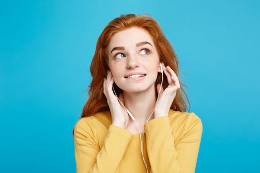 Lifestyle concept - Portrait of cheerful happy ginger red hair girl enjoy listening to music with headphones joyful smiling to camera. Isolated on Blue Pastel Background. Copy space.