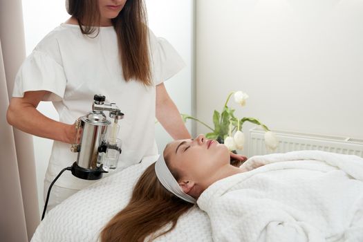 The procedure of steaming the skin of the face of a young woman before cleaning the skin in spa salon
