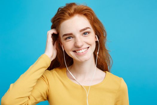 Lifestyle concept - Portrait of cheerful happy ginger red hair girl enjoy listening to music with headphones joyful smiling to camera. Isolated on Blue Pastel Background. Copy space.