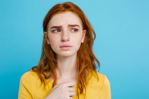 Headshot Portrait of tender redhead teenage girl with serious expression looking at camera. Caucasian woman model with ginger hair posing indoors.Pastel blue background. Copy Space.