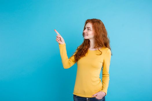 Close up Portrait young beautiful attractive redhair girl happy with something and pointing finger. Blue Pastel Background. Copy space.