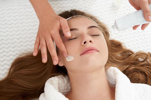 Cosmetologist applying cream on patient face, portrait closeup view. Woman in beauty clinic with doctor beautician