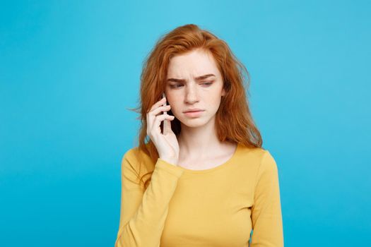 Lifestyle concept - Portrait of ginger red hair girl with shocking and stressful expression while talking with friend by mobile phone. Isolated on Blue Pastel Background. Copy space.