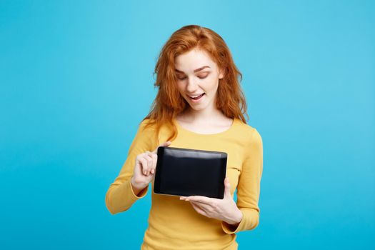 Business Concept - Close up Portrait young beautiful attractive redhair girl smiling showing digital tablet screen on black. Blue Pastel Background.