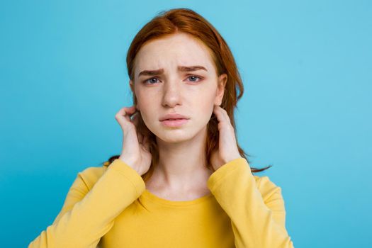 Headshot Portrait of tender redhead teenage girl with serious expression looking at camera. Caucasian woman model with ginger hair posing indoors.Pastel blue background. Copy Space.