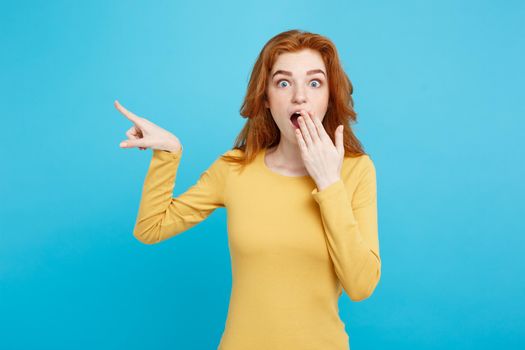 Close up Portrait young beautiful attractive redhair girl with shocking with something and pointing finger. Blue Pastel Background. Copy space.