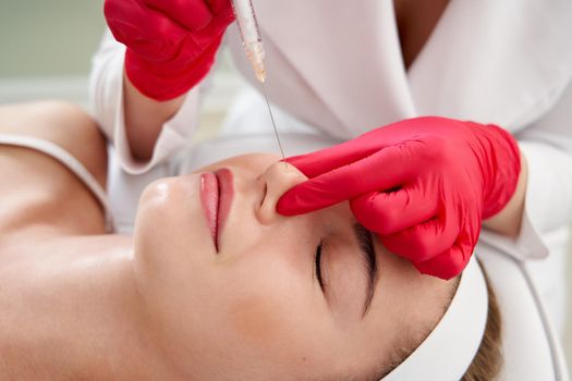 Beautician making injection in the nose with syringe in beauty salon. Cosmetic rejuvenating facial treatment