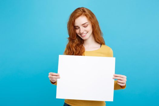 Close up Portrait young beautiful attractive ginger red hair girl smiling showing blank sign. Blue Pastel Background. Copy space.