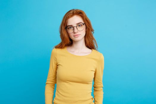 Headshot Portrait of tender redhead teenage girl with serious expression looking at camera. Caucasian woman model with ginger hair posing indoors.Pastel blue background. Copy Space.