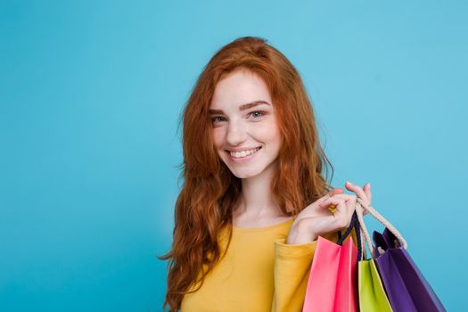 Shopping Concept - Close up Portrait young beautiful attractive redhair girl smiling looking at camera with shopping bag. Blue Pastel Background. Copy space.