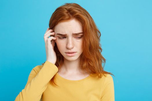 Headshot Portrait of tender redhead teenage girl with serious expression looking at camera. Caucasian woman model with ginger hair posing indoors.Pastel blue background. Copy Space.