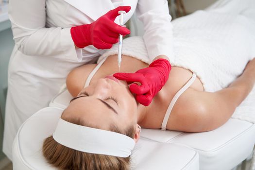 Beautician making injection in the chin with syringe in beauty salon. Cosmetic rejuvenating facial treatment