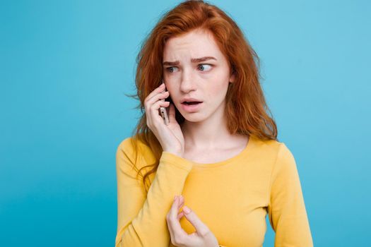 Lifestyle concept - Portrait of ginger red hair girl with shocking and stressful expression while talking with friend by mobile phone. Isolated on Blue Pastel Background. Copy space.