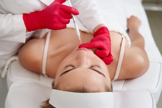 Beautician making injection in the chin with syringe in beauty salon. Cosmetic rejuvenating facial treatment