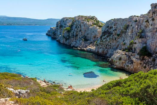 Marathopoli, Greece - August29, 2019: People swimming in the clear blue waters of Proti Island, near Marathopoli, Messinia at Peloponnese. The name of the island derives from the ancient sea god Proteus, son of Poseidon.