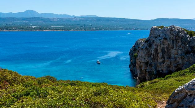 Boat swimming in the clear blue waters of Proti Island, near Marathopoli, Messinia at Peloponnese. The name of the island derives from the ancient sea god Proteus, son of Poseidon.