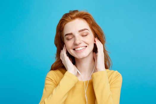 Lifestyle concept - Portrait of cheerful happy ginger red hair girl enjoy listening to music with headphones joyful smiling to camera. Isolated on Blue Pastel Background. Copy space.