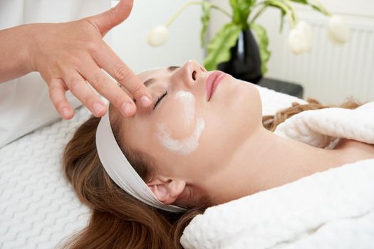 Cosmetologist applying cream on patient face, portrait closeup view. Woman in beauty clinic with doctor beautician