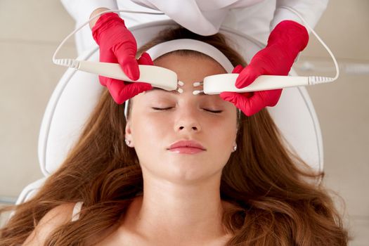 Beautiful Woman At Spa Clinic Receiving Stimulating Electric Facial Treatment From Therapist. Closeup Of Young Female Face During Microcurrent Therapy