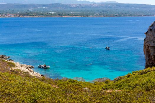 People swimming in the clear blue waters of Proti Island, near Marathopoli, Messinia at Peloponnese. The name of the island derives from the ancient sea god Proteus, son of Poseidon.