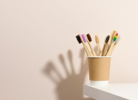 wooden toothbrushes in a paper cup on a white table. Beige background, zero waste